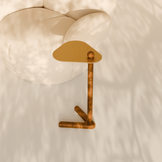 Trilo side table with sculptural teak wood base and brass-finished top beside a arm chair.