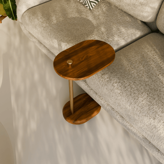Minimal C-shaped side table handcrafted from solid teak wood with a brushed brass knob, placed beside a sofa.